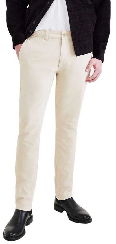 Man met beige chino broek, wit t-shirt en zwart geruit jasje. Zwarte schoenen.