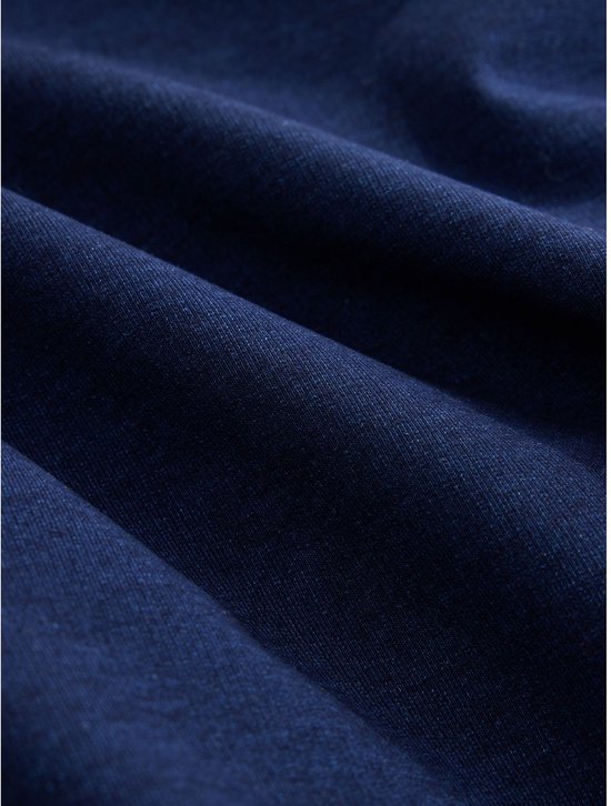 Gedetailleerde close-up van de donkerblauwe denimstof met zichtbare textuur en plooien.