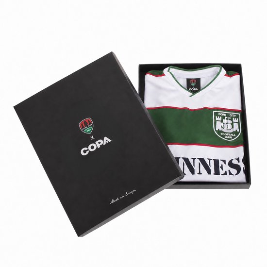 Wit, groen en rood voetbalshirt van Cork City FC, met "INNESS" op de voorkant, in een zwarte geschenkdoos.