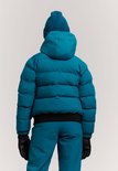 Achterkant van een meisje in blauwe ski-jas, muts, broek en zwarte handschoenen. Zwarte band onderaan de jas.