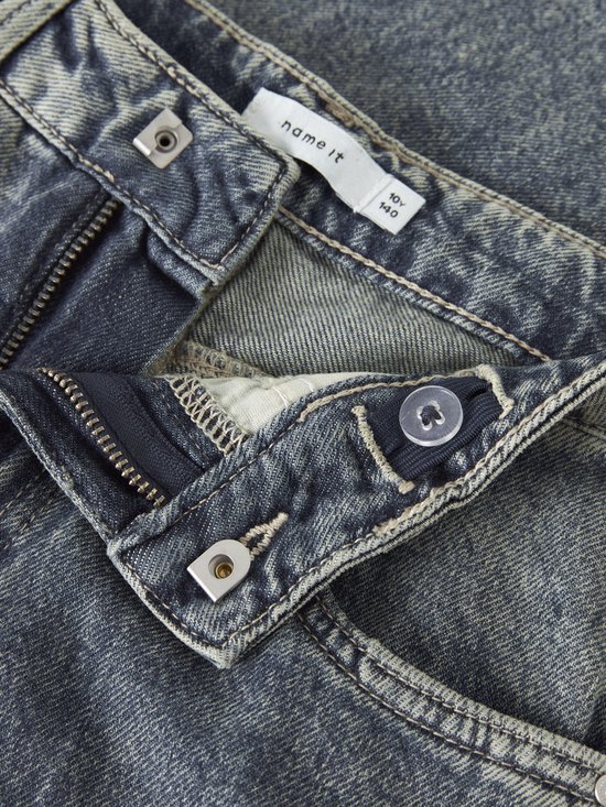 Sluiting van een lichtblauwe wijde jeans: knopen, ritssluiting, en verstelbare tailleband met knoopje.