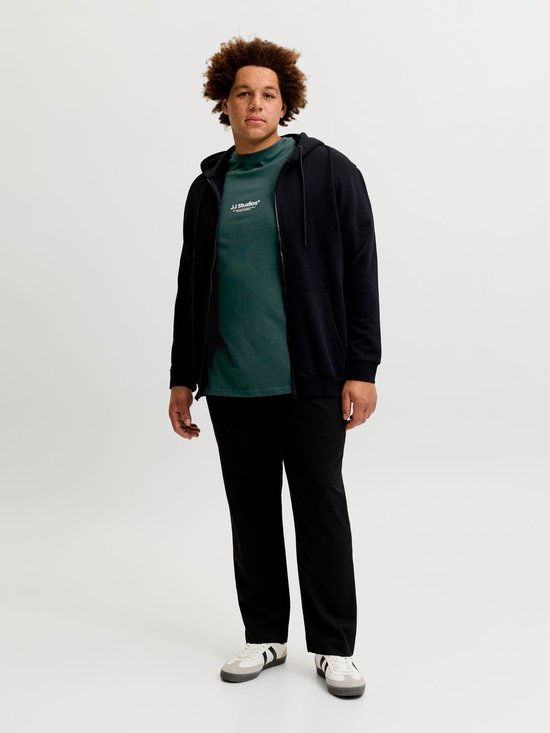 Man met krullend haar, gekleed in een donkergroen T-shirt met 'JJ Studios' tekst en een zwarte hoodie.