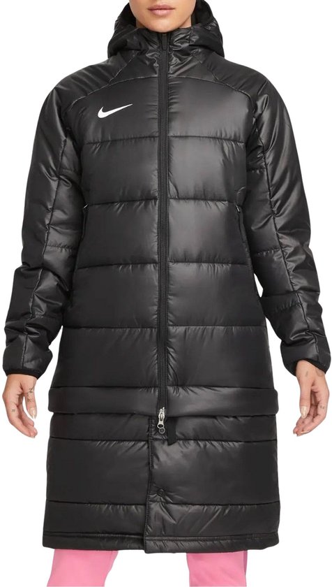 Zwarte Nike winterjas voor dames, van voren gezien, met capuchon en horizontale naden. Een vrouw draagt de jas met een roze broek. Nike logo op de borst.