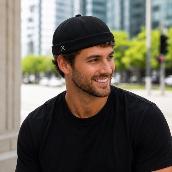 Man lacht en kijkt weg, draagt een zwarte Docker pet met 'X'-detail op de omgeslagen rand.