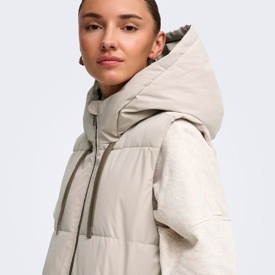 Close-up van een model in een lange, lichtgrijze gewatteerde bodywarmer met capuchon.