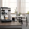 Zilverkleurige De'Longhi Magnifica EVO volautomatische espressomachine met een glas cappuccino en een kop zwarte koffie op een aanrecht.