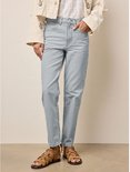 Vrouw in een lichtgrijze gestreepte mom jeans met rechte pijpen, witte top en bruine sandalen.