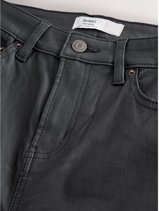 Detail van de tailleband van een zwarte skinny jeans met coating, met knopen en zak.