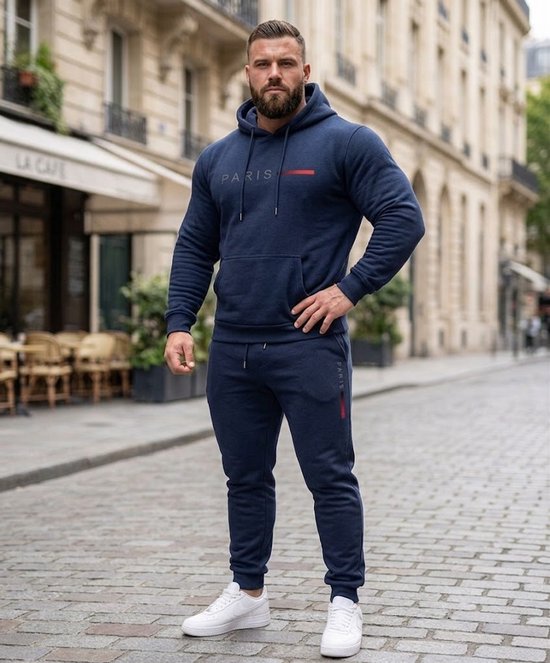 Man met donkerblauwe trainingsset: hoodie met "PARIS" opdruk en joggingbroek. Op straat.