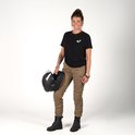 Vrouw met bruin haar in een knot, staand met een zwarte T-shirt en zandkleurige cargobroek, houdt een helm vast.