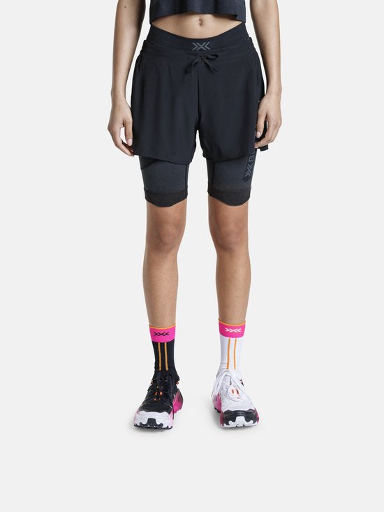 Une femme porte un ensemble de sport noir avec un short, un cuissard court moulant 'X BIONIC' et des chaussettes colorées.