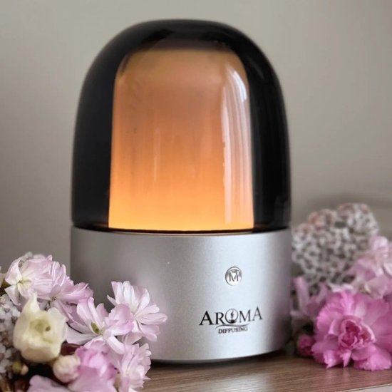 Zilverkleurige aroma diffuser met glanzende zwarte kap, omringd door zachtroze en witte bloemen.