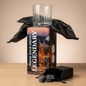 Een whiskeyglas op een doos met afbeeldingen van whiskey en stenen, omringd door zwart tissuepapier.