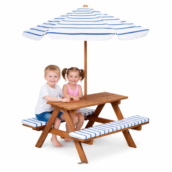 Houten picknicktafel voor kinderen met blauw-wit gestreepte kussens en parasol. Jongen en meisje zitten op de bankjes.