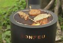 Zwart BonFeu tuinhaard met grill, met daarop een worst en satéspiesjes.