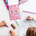 Meisje kleurt een zeemeermin en kat met paarse stift. Liggend op tafel liggen gekleurde potloden.