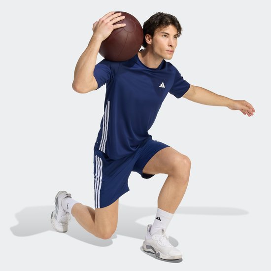 Man met bal op schouder, draagt donkerblauw T-shirt met witte Adidas strepen op de zijkanten.