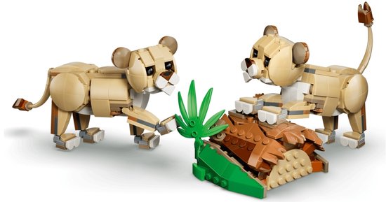 Twee LEGO leeuwenwelpen van bruine en beige stenen, spelend met een stuk hout op een groene ondergrond met bloemen.
