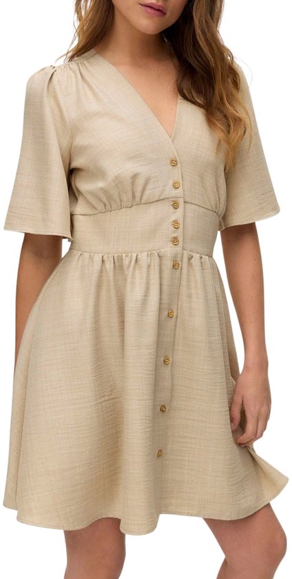 Model in beige jurk met V-hals, korte pofmouwen en knoopjes. Elastische tailleband en een zwierige rok.