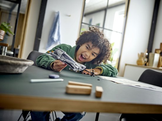 Jongen speelt met grijze LEGO Star Wars snub fighter, met minifiguren en instructies op tafel.