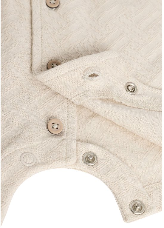 Close-up van de onderkant van een beige babyromper met visgraatpatroon en drukknoopjes.