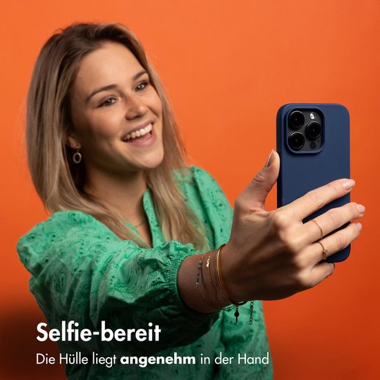Vrolijke vrouw neemt selfie met donkerblauwe telefoonhoes. 'Selfie-bereit'. De hoes ligt aangenaam in de hand.