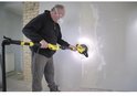 Een man met veiligheidsbril en mondkapje schuurt een muur met een gele en zwarte telescoopschuurmachine.