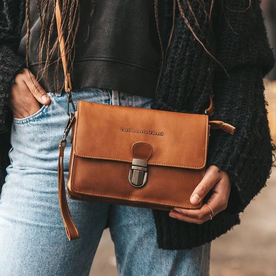 Een cognac kleurige leren schoudertas van The Chesterfield Brand, gedragen door een model met blauwe jeans en een zwarte fluffy jas.