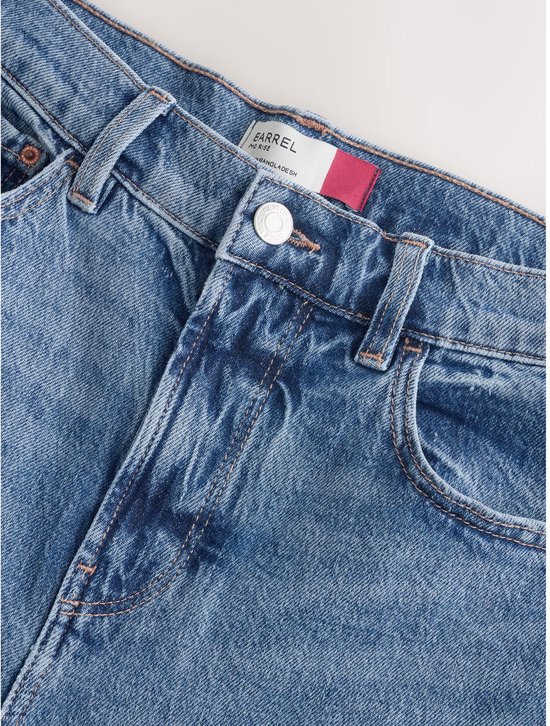 Sluiting van een blauwe jeans met een knoop en ritssluiting, het merk 'Next' is zichtbaar op het label.