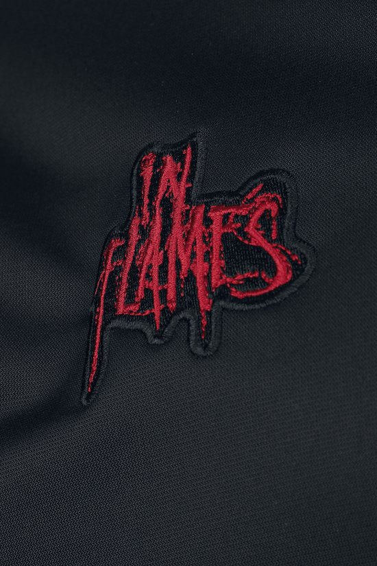 Close-up van rode 'In Flames' bandlogo opdruk op een zwarte trainingsjas.
