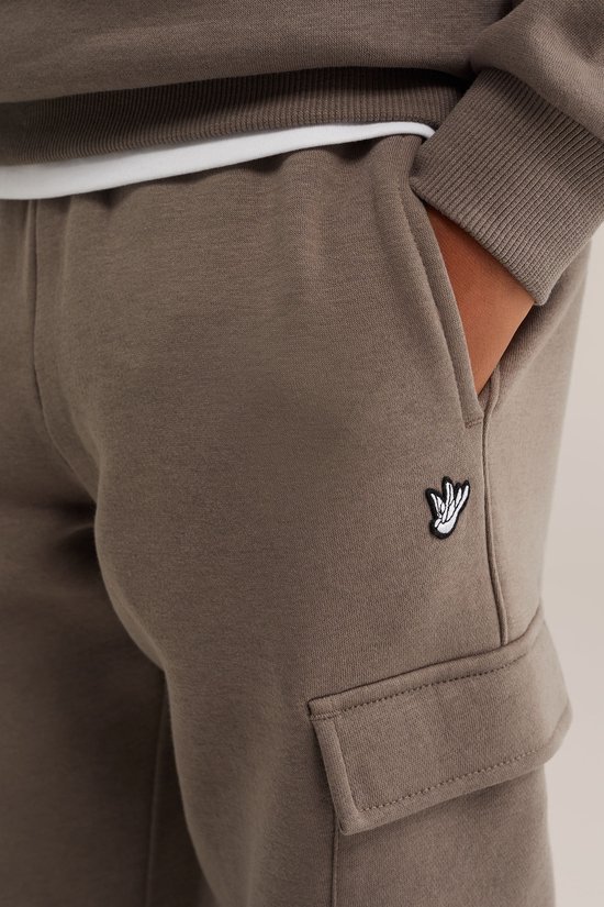 Detail van bruine joggingbroek met cargo zak en klein logo op de zijkant.
