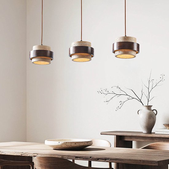Trois lampes suspendues avec des corps tubulaires en travertin et des anneaux en bois foncé sont suspendues au-dessus d'une table en bois.