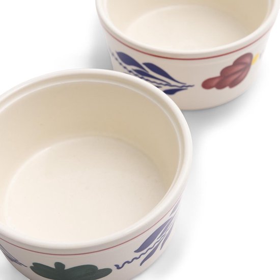 Twee crème ramkinkjes met rode en blauwe bloemen en bladeren decoratie.