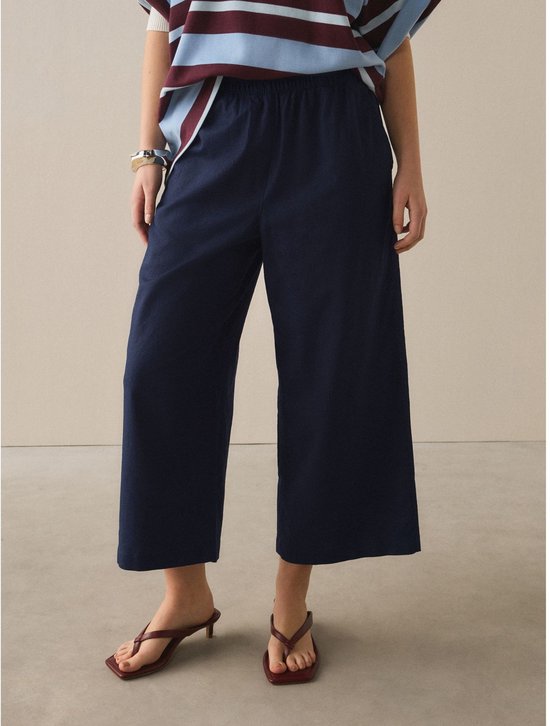 Model draagt donkerblauwe wijde broek met elastische tailleband, gecombineerd met gestreept shirt en bruine sandalen.