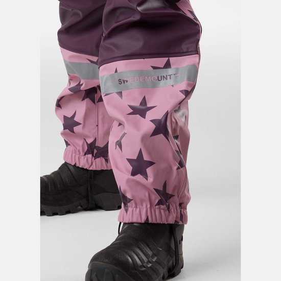 Close-up van de roze regenbroek met donkerpaarse sterrenprint, met reflecterende banden op de onderbenen en zwarte laarzen.