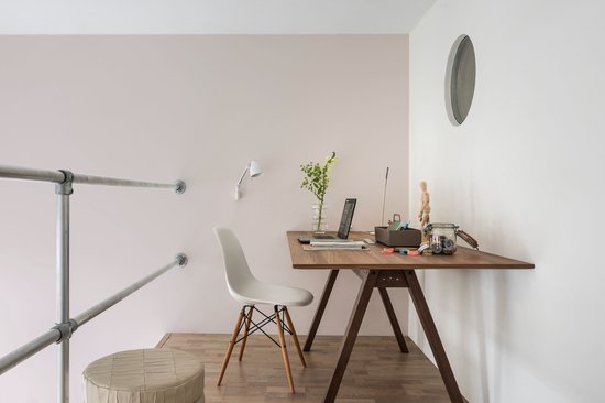 Bureauhoek met een houten bureau, witte stoel, laptop en een schuine wand met reling.