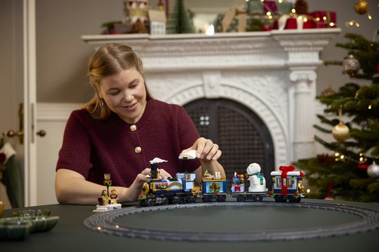 Vrouw bouwt aan een LEGO-trein met kerstdecoraties, bij een kerstboom.