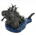 Grijze Godzilla figuur met scherpe rugplaten, op een blauwe waterbasis, van opzij gezien.