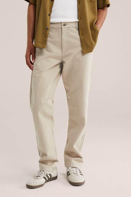 Model met handen in de zakken van een beige chino broek en olijfgroen hemd.