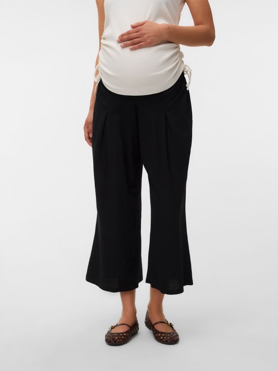 Detail van zwarte, wijde, cropped zwangerschapsbroek met plooien, gedragen door een zwangere vrouw.