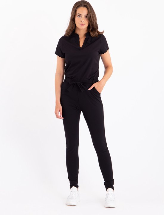 Model met zwarte broek met strikceintuur en zwarte blouse met V-hals.