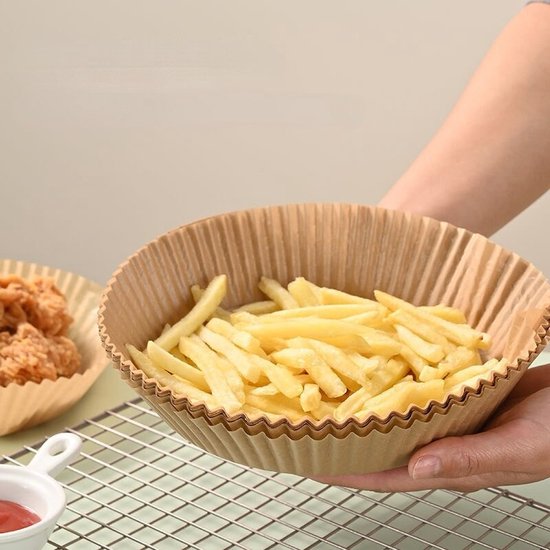 Papieren airfryer bakvormpjes gevuld met frietjes, vastgehouden door een persoon.