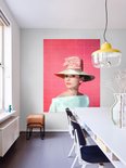 Audrey Hepburn portant un grand chapeau avec un nœud rose sur fond rose.