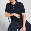 Man zit, draagt een donkerblauwe poloshirt met korte mouwen, donkerblauwe kraag, donkere broek.