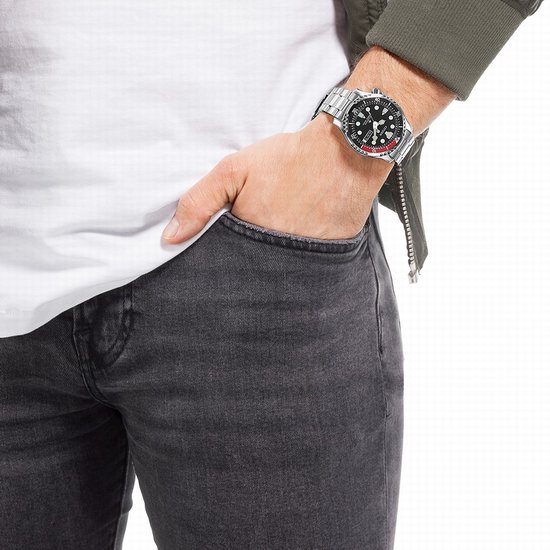 Man met witte T-shirt en groene jas draagt een Citizen duikhorloge om de pols.