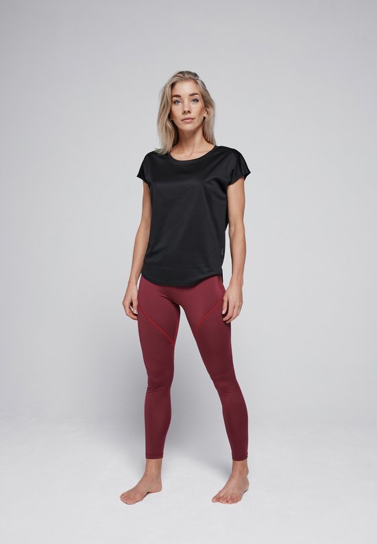 Model met blonde haren, draagt een zwarte sporttop met korte mouwen en een rode legging. Ze staat met haar handen omhoog.