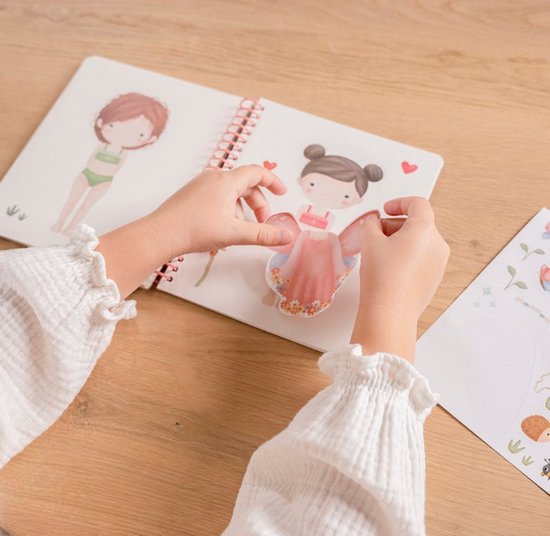 Kind plakt een jurk op een getekend meisje in een schetsboek. De jurk is roze met bloemen.