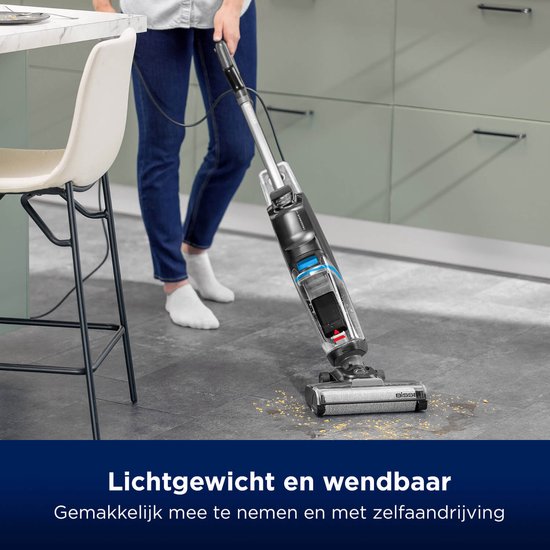 Een persoon met spijkerbroek en witte sokken gebruikt de lichte, wendbare BISSELL CrossWave vloerreiniger op een grijze tegelvloer.