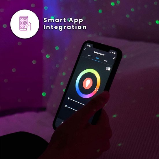 Een hand houdt een smartphone met een app voor galaxy projector. De app toont een kleurencirkel en instellingen. Groene stippen op de muur.