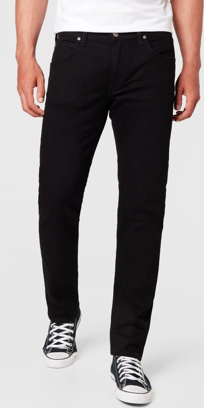 Man in een wit T-shirt en zwarte jeans, draagt zwarte sneakers met witte strepen.